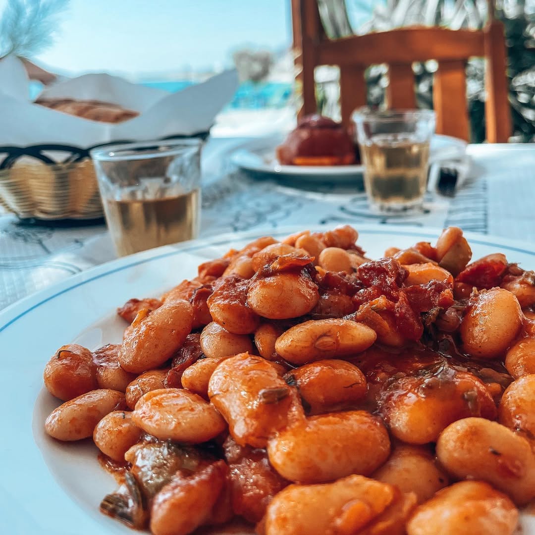 Sunset dining experience at Gorgona Taverna with fried seafood platter, Artemis ouzo bottles, and traditional Greek atmosphere against backdrop of calm sea and boats
